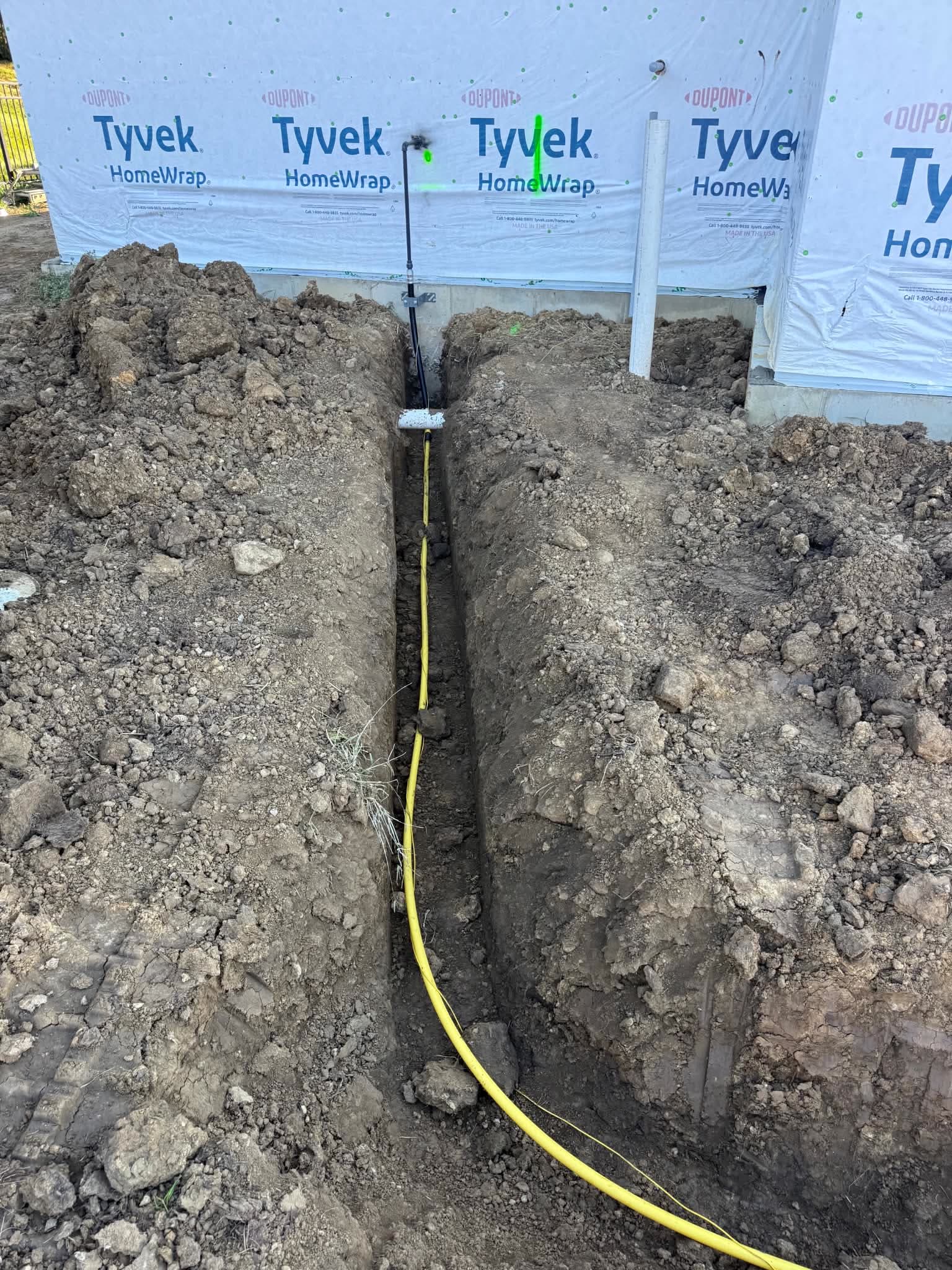 A narrow trench with yellow gas line run to a new foundation